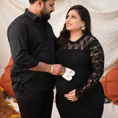 A classic couple's pose with a sweet touch. Dressed in elegant black, the couple holds a tiny pair of baby shoes against the bump, a beautiful symbol of the little one they are eagerly awaiting.
