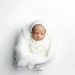 Wrapped in pure white, this 18-day-old newborn rests peacefully. My minimalist newborn photography focuses on their serene beauty and delicate features, creating a clean and timeless portrait.