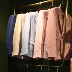A rack of our tailored blazers in various lightweight fabrics and colors, including linen and seersucker. This collection is designed for refined casual wear, perfect for warmer climates.