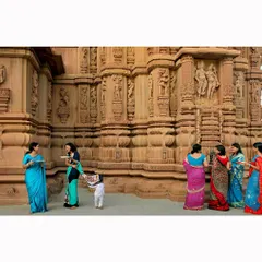 Women in colorful sarees gather outside a temple with intricately carved walls. This image from the Aditya Birla Group series documents a moment of social gathering and celebration within a sacred space.