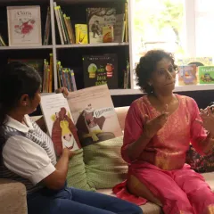 A volunteer uses expressive gestures to narrate a story to a child at our 'Sea of Stories' library. Our storytellers don't just read; they use their whole bodies to convey emotion and action, making the tale accessible and engaging for children with hearing impairments.