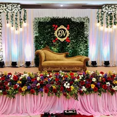 An elegant and classic reception stage combining a rich floral border with a modern green wall backdrop. We added a personalized, illuminated monogram for the couple, 'DV', making the design truly unique to their story.