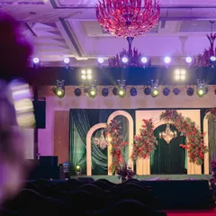 The stage for this modern Sangeet featured a backdrop of emerald green velvet and elegant gilded arches, asymmetrically decorated with crimson floral arrangements for a contemporary, artistic feel.