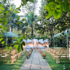 Framed by lush leaves, this view captures the scale and beauty of a wedding ceremony at Farmhouse Collective. The stone pathway leads guests' eyes to the beautifully decorated stage.
