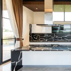 A close-up of the kitchen island, made from a single piece of black marble with dramatic white veining. The island incorporates a cooktop, making it a central hub for cooking and socializing.