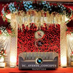 A classic and romantic wedding reception stage, enveloped in a wall of rich red roses and elegant white florals. The dramatic draping and warm lighting create an atmosphere of pure romance.