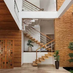 A view of the staircase in the Cube House, set against a double-height space with a stone-clad wall. The combination of wood treads, steel railings, and glass creates a modern and airy feel, connecting multiple levels of the home.