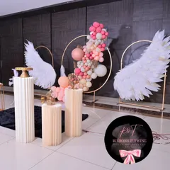 The main photo stage with our signature angel wings, a circular balloon garland, and fluted pedestals for the cake and decorative items.