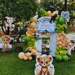 We transformed this garden into a wild jungle adventure for a first birthday. The setup includes an organic balloon arch in earthy tones, a custom 'Into the Wild at One' backdrop, and adorable cutouts of jungle animals like lions, monkeys, and giraffes.