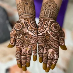 This symmetrical design features bold circular motifs and intricate line work. The solid henna on the fingertips provides a classic contrast to the detailed patterns on the palms.