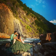 A romantic moment by the river, with the warm sunlight highlighting the couple against the dramatic mountain cliffs.