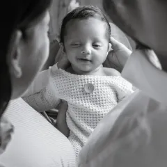 A little wink for the camera. This close-up black and white shot captures the adorable personality of this newborn, framed by his loving parents.