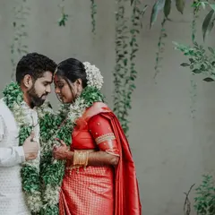 A beautiful portrait of the couple sharing a quiet moment, showcasing the elegance of the bride's red silk saree and the traditional flower garlands.