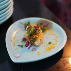 A single, perfectly crafted piece of sev puri. Garnished with fresh pomegranate, onion, and fine sev, this bite-sized snack represents our commitment to elevating even the simplest street food dishes.