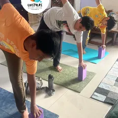 A group of young boys practice a modified Half Moon Pose using blocks for support. This helps them build balance, concentration, and body awareness.