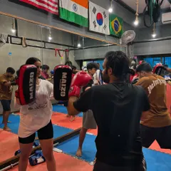 A student practices her striking on the pads during a group kickboxing class. This drill is essential for developing power, timing, and proper form in a controlled environment.
