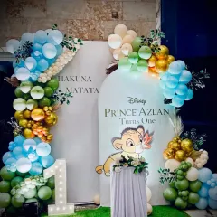 A "Hakuna Matata" themed first birthday party based on Disney's The Lion King. The setup includes a custom backdrop with baby Simba, balloon arches in jungle colors, and a light-up "1" marquee number to celebrate the big milestone.