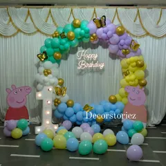 A complete Peppa Pig party setup perfect for a first birthday. This features a full balloon ring in pastel colors, life-sized character cutouts, a light-up marquee number '1', and a custom 'Happy Birthday' neon sign for that extra glow.