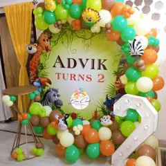 A full jungle-themed balloon backdrop for a second birthday. This decoration uses a mix of orange, green, and brown balloons with lots of animal cutouts for a rich, layered look.