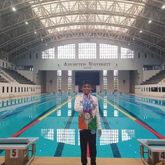 This is the result of dedication. Here is our swimmer, Bryce, proudly displaying his gold, silver, and bronze medals at the Asian Open Schools Invitational Swimming Championship in Thailand. This image captures the proud moment of achievement at a world-class swimming facility, a goal we help our competitive swimmers reach.
