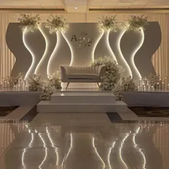 This modern reception stage features a custom-designed backdrop with undulating waves and integrated backlighting. The minimalist sofa and clean white florals create a chic and contemporary look.