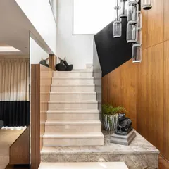 The same staircase, showing its elegant proportions and the beautiful contrast between the light marble, dark railing, and warm wood wall. It's a perfect example of a transitional space designed with intention.