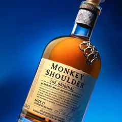 An experimental shot of a Monkey Shoulder whiskey bottle. The dynamic angle and bold blue background lighting make the bottle feel modern and exciting, perfect for social media or ad campaigns.