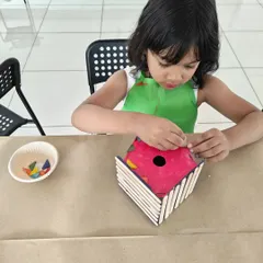 I love seeing the concentration on their faces! Here, a young artist is carefully assembling her own colorful birdhouse, a perfect take-home creation.