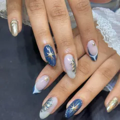 This elegant design features hand-painted gold stars and intricate fan-like patterns over a deep blue and sheer base. It's a sophisticated take on celestial nail art.