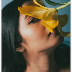 Using props like flowers can add a layer of poetry to a beauty shot. Here, the yellow lily partially obscures the model's face, creating a sense of mystery and artistry. The cool blue background contrasts beautifully with the warm tones of the flower and skin.