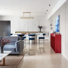 A glimpse into an open-plan living and dining area where modern design meets vibrant personality. The striking red console and rich blue velvet chairs add a bold splash of color, showcasing how we tailor each space to reflect our client's unique style while maintaining a cohesive, elegant flow.