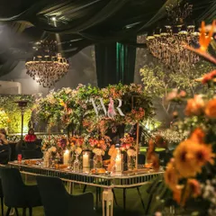 A romantic tablescape from a 'Garden of Dreams' engagement. The mirrored table reflects the glow of candles and the lush, colorful floral arrangements, all set under a canopy of green drapes and sparkling chandeliers.