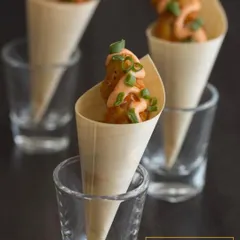 These are crispy fried vegetable balls served in paper cones with a drizzle of spicy mayo. This presentation makes them easy for guests to enjoy while socializing at cocktail parties or corporate events.