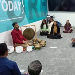 A corporate team begins their journey inward. Participants are seated in a comfortable meditative posture, preparing their minds for the immersive sound bath experience in their own office environment.