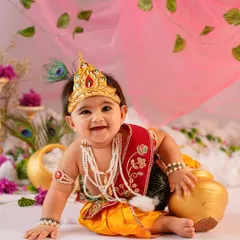 This little Krishna, with his sweet smile and traditional attire, leans against a golden pot. Our Janmashtami sessions are filled with authentic props to make the theme come alive.