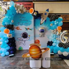 A fun, cartoon-style astronaut theme for a 6th birthday, complete with planet cutouts, a silver astronaut figure, and a bright blue balloon arch.