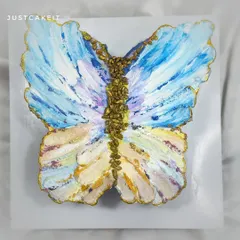 A butterfly-shaped cake decorated with an abstract, impressionistic painting style using buttercream. The gold details add a touch of elegance to this artistic chocolate truffle cake.