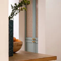 This modern pooja room features green shaker-style shutters with rattan and glass inserts. The brass knobs add a final touch of sophistication, creating a spiritual space that is serene and stylish, not overtly traditional.