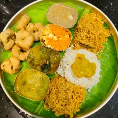 A traditional meal served on a banana leaf, featuring various dishes prepared for a festival. This includes vade, payasa, and different kinds of rice.