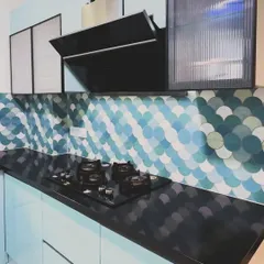 The cooking area of the pastel blue kitchen, featuring a four-burner hob on a black granite countertop. The fluted glass on the upper cabinets adds a touch of texture and elegance to the colorful design.