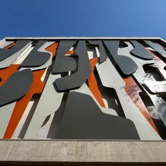 A low angle view of the "Framed Austerity" facade against a clear blue sky. The artwork's layers of grey, white, and orange create a powerful graphic statement, showcasing how I use art to give a building a unique identity.