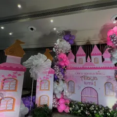 This princess castle backdrop sets the stage for a royal celebration. The pink castle is flanked by towers and a cascading balloon garland in shades of pink, purple, and white.