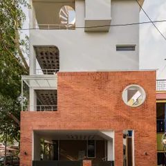 For this urban home in Bangalore, we contrasted a clean white facade with the raw texture of rat-trap bond brickwork. The circular window and spiral staircase are not just design elements; they are invitations to explore the different levels and how light moves through the space.