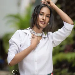 A confident and direct outdoor portrait. The natural setting adds a layer of authenticity, while her strong gaze and classic styling create a timeless look.