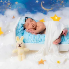 A peaceful newborn dreams amongst the stars and clouds in this creative celestial-themed setup, complete with a tiny bed and a knitted bunny friend.