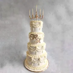 For this beautiful wedding, we created a four-tier cake with traditional Lambeth piping. The topper was a custom-made candle stand, inspired by the chandelier at the venue, to make it truly personal for the couple.