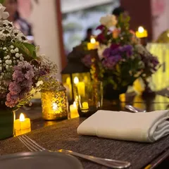 A close-up of the candlelit table setting. The warm glow of the candles and lanterns creates a cozy and romantic atmosphere.