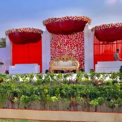 A daytime view of a spectacular outdoor wedding stage. The vibrant red floral arrangements and drapery stand out beautifully against the open sky, creating a powerful and photogenic setting.