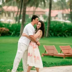 A tender kiss on the forehead, set against the soft-focus background of a lush green resort, creating a classic romantic portrait.
