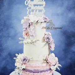 A beautiful three-tiered cake designed for a 25th wedding anniversary. The cake features a soft lavender and pink ombre ruffle effect on the bottom tier, topped with delicate, handcrafted sugar flowers.